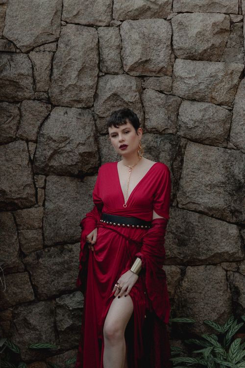 Free A stylish woman in red dress standing confidently against a textured stone wall. Stock Photo
