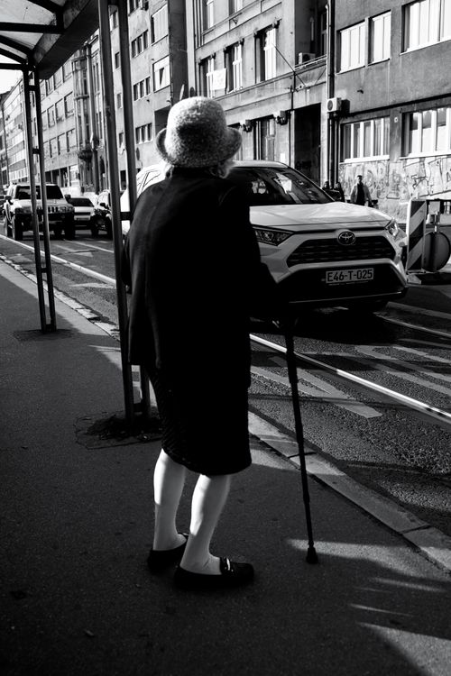 Free Striking black and white street scene of an elderly woman waiting at a bus stop in Sarajevo. Stock Photo