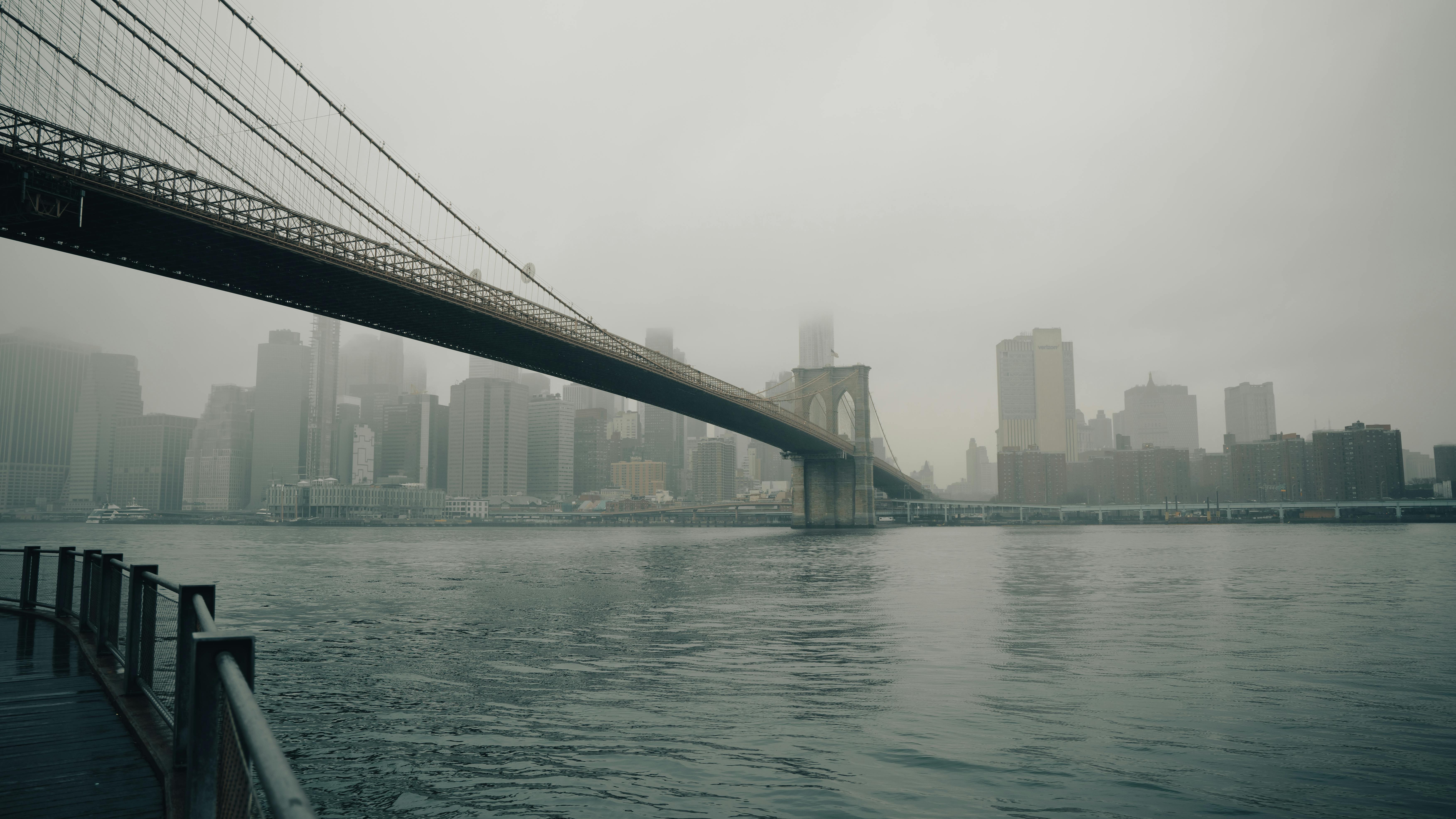 Moody view of Brooklyn Bridge with fog obscuring New York City's skyline.