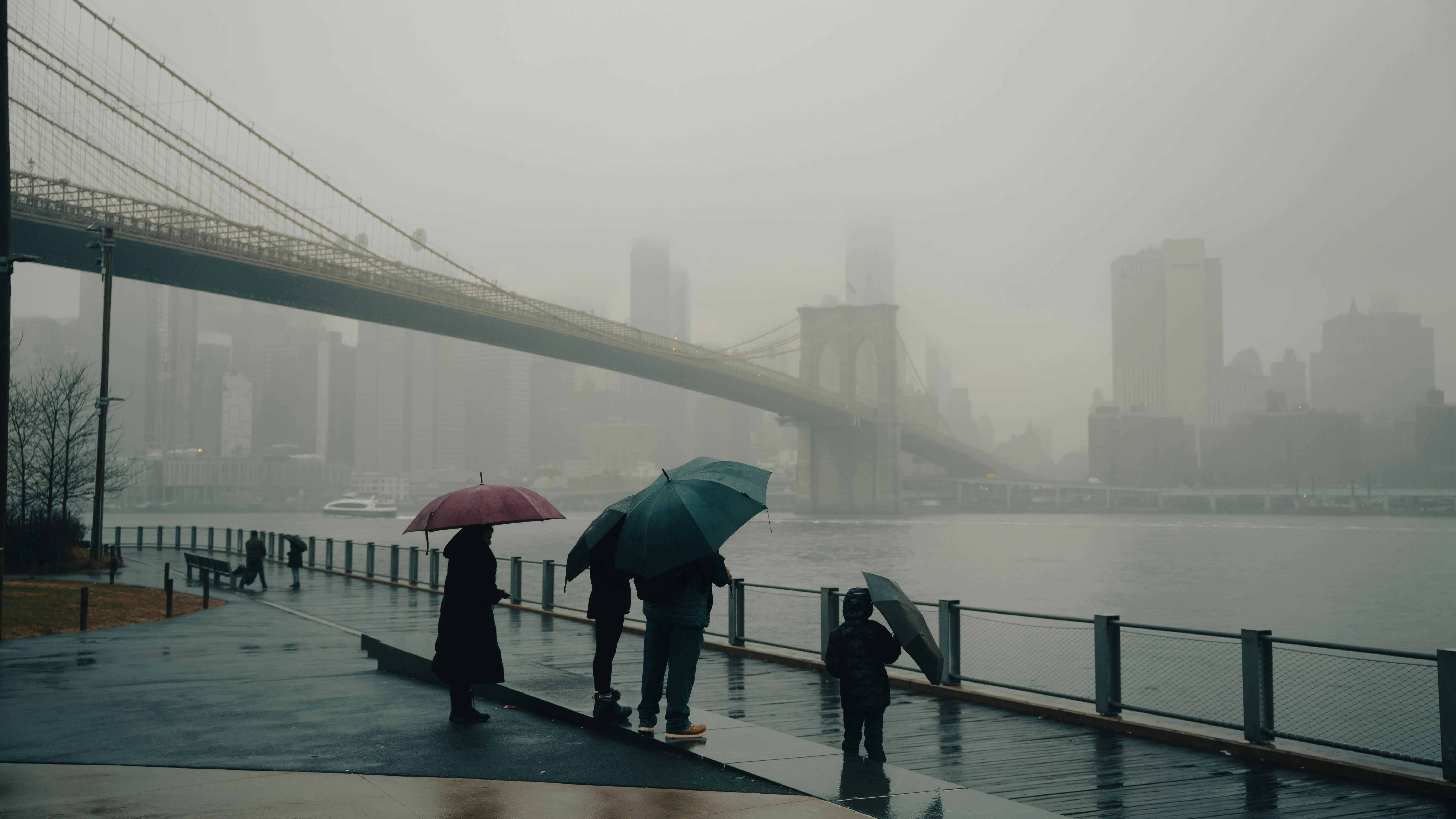 People with umbrellas viewing the foggy Brooklyn Bridge in New York City.