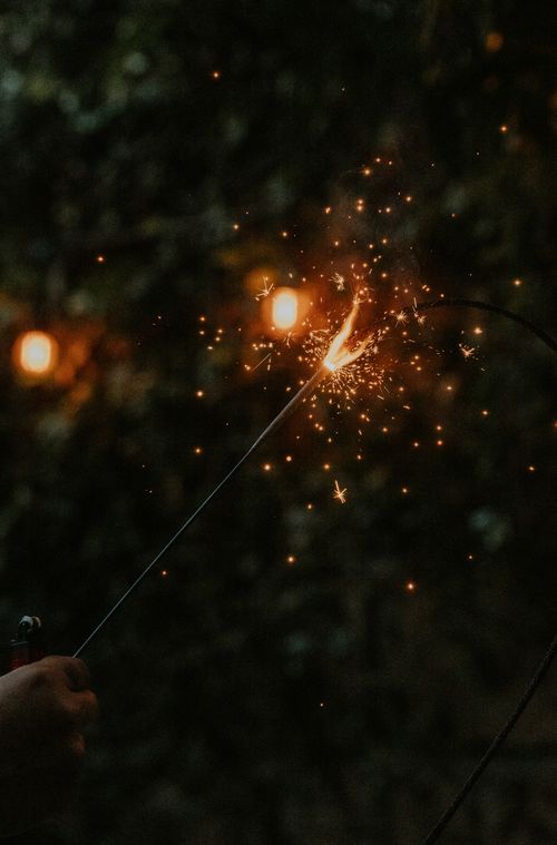 Free A person holding a lit sparkler at night, emitting bright sparks and glow against a dark background. Stock Photo