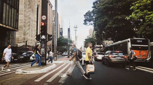 Free Urban scene with people crossing a vibrant city intersection amid traffic and buildings. Stock Photo