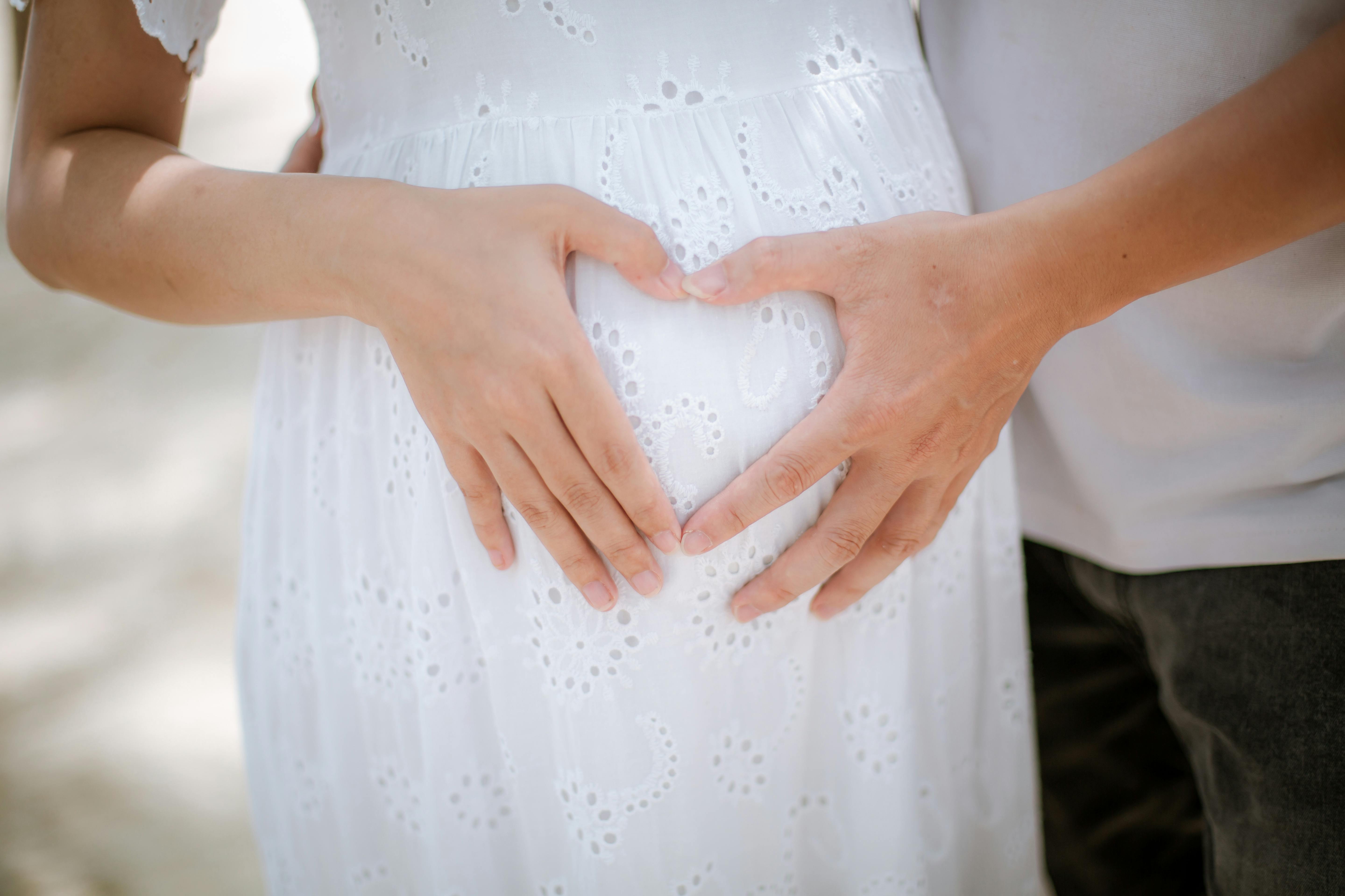A touching maternity photo on Da Nang beach with loving hands forming a heart over a baby bump.