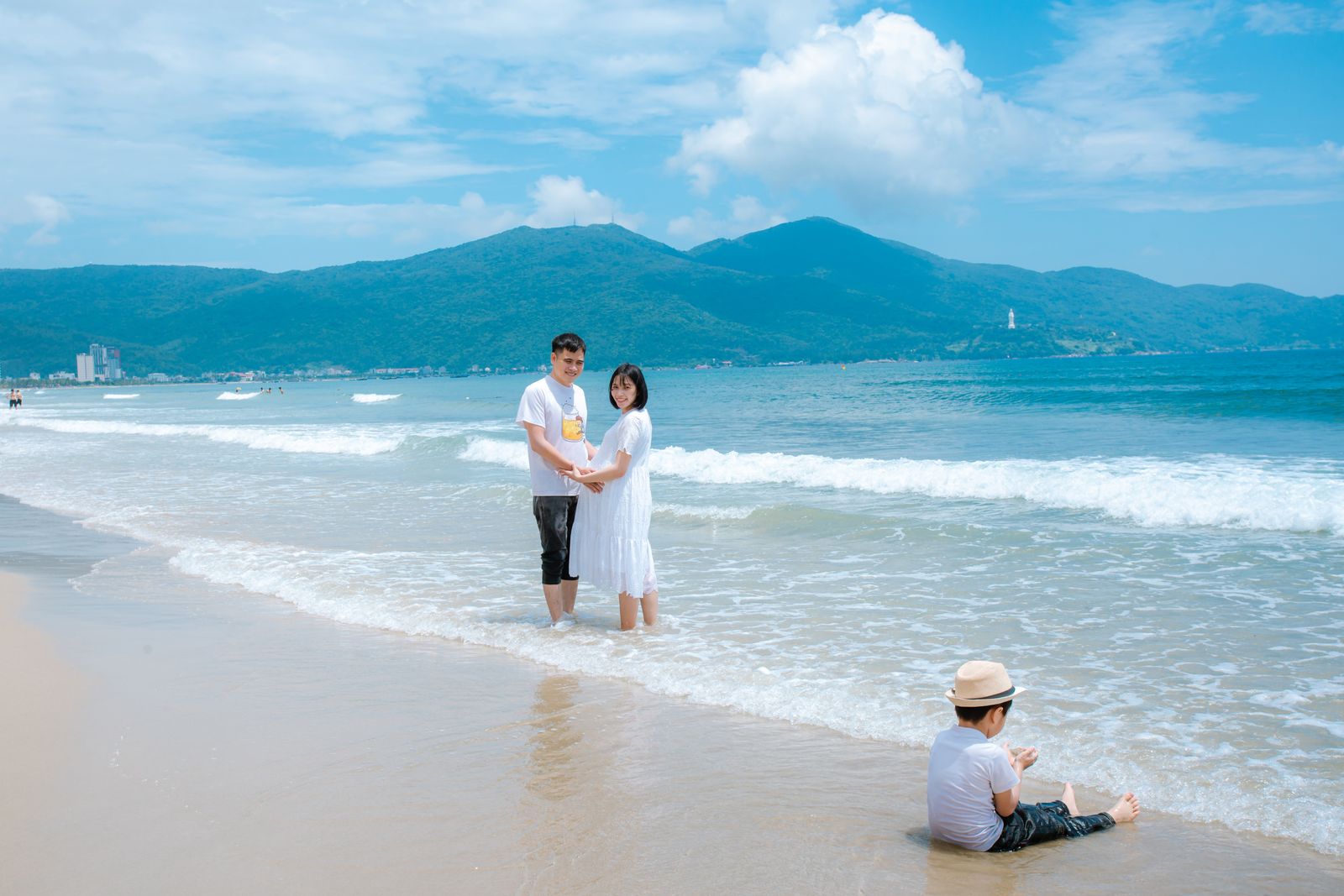 Family enjoying a sunny day at Da Nang Beach, Vietnam with mountains in the background.