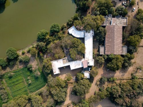 Free Aerial shot of a unique architectural building surrounded by trees and near a lake, offering a blend of nature and design. Stock Photo