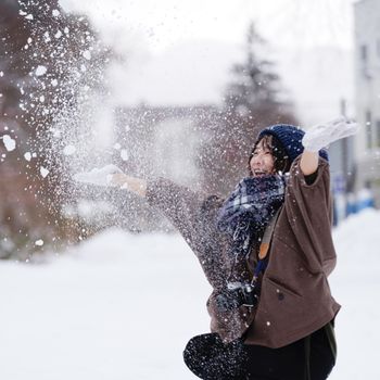 A joyful woman enjoys playing with snow on a cold winter day, capturing the essence of fun outdoors.