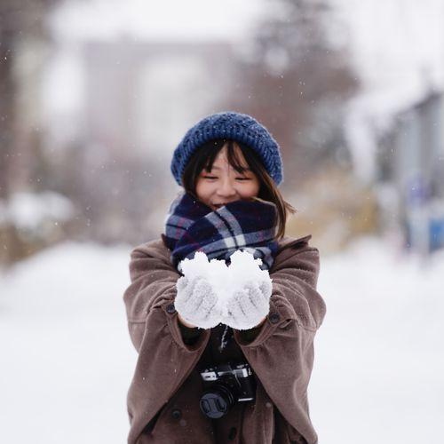 Free A cheerful woman holding snow, enjoying a snowy winter day outdoors. Stock Photo