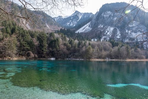 Free A serene alpine lake surrounded by winter trees and snow-capped mountains, reflecting nature's tranquility. Stock Photo