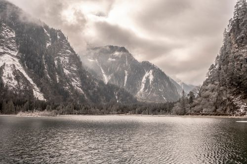 Free Peaceful alpine lake surrounded by snow-capped mountains under a cloudy sky. Stock Photo