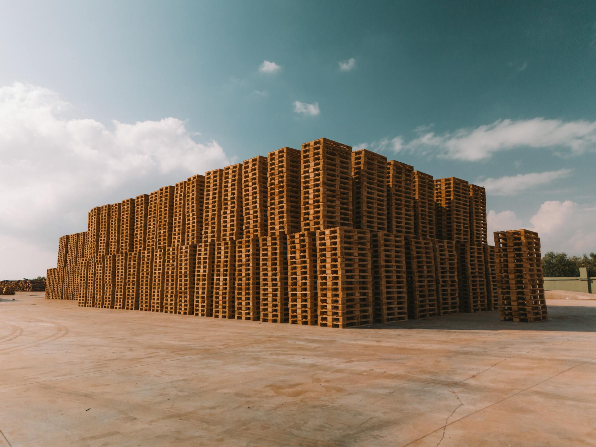 Large stacks of wooden pallets under a partly cloudy sky on a sunny day.