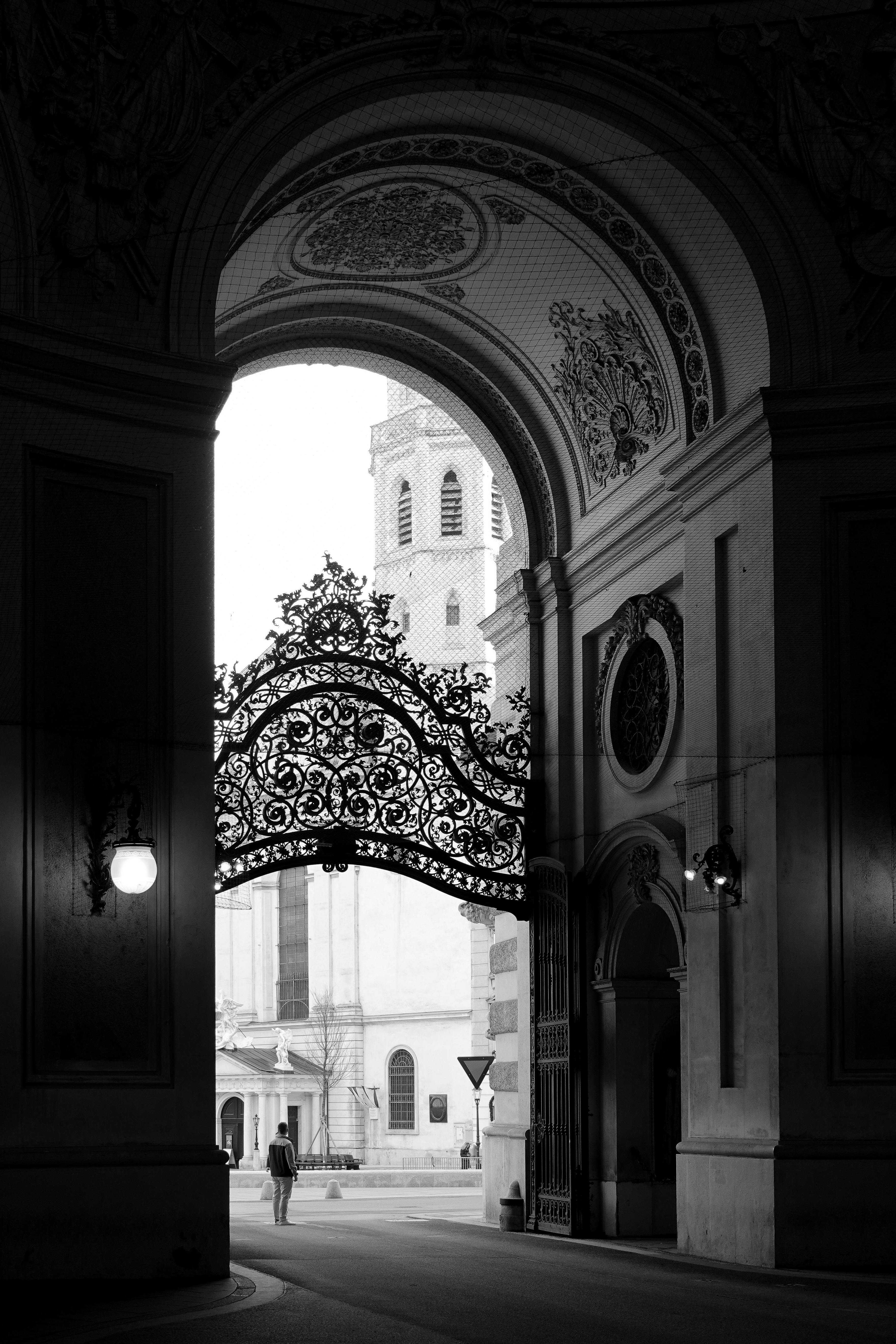 Black and white image of an ornate archway framing a historic cityscape beyond.