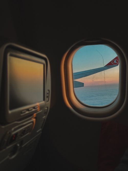 Free Scenic view of an airplane wing over clouds at sunrise, captured through a window. Stock Photo