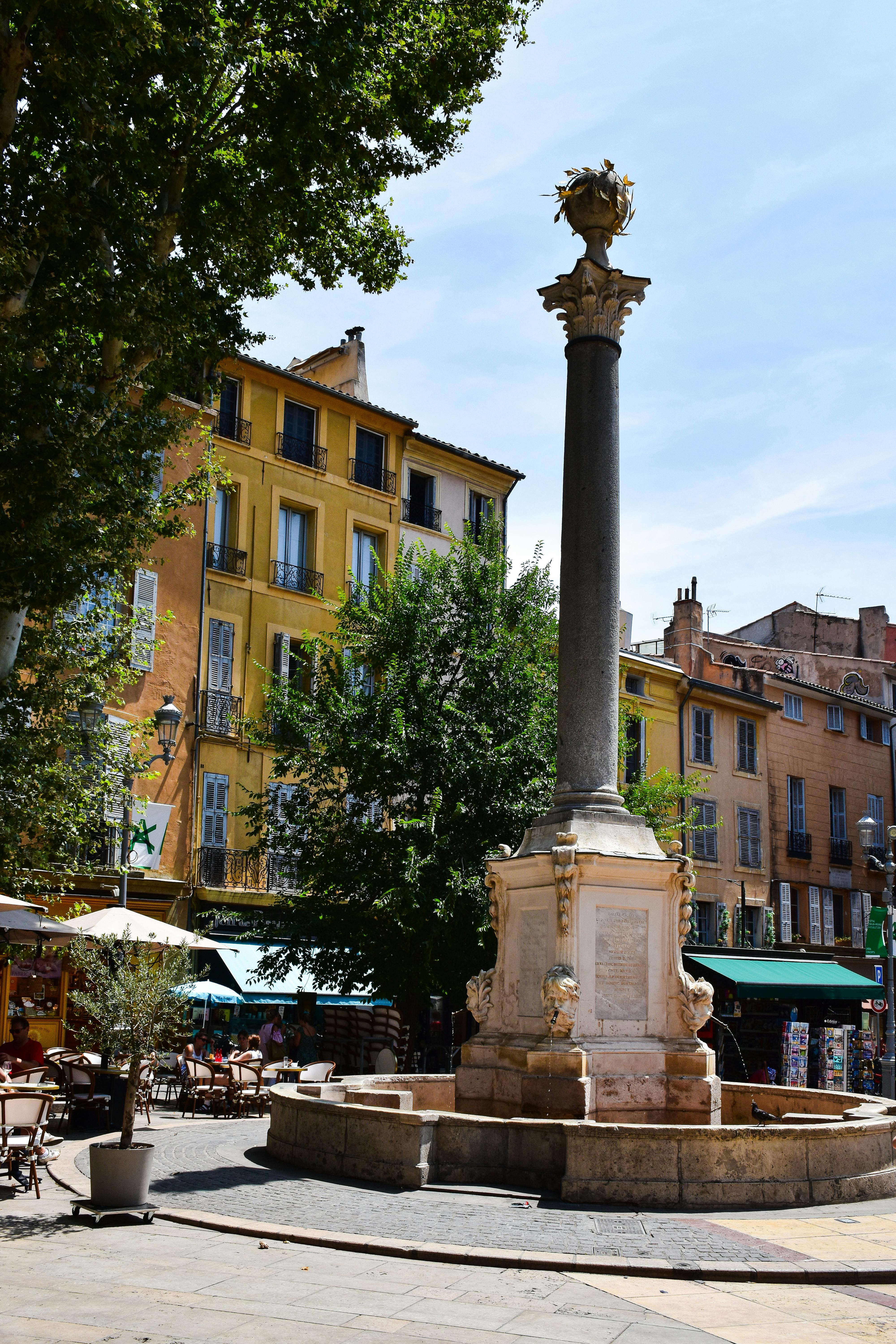 Sunny day in a picturesque square with a historic column fountain in Aix-en-Provence, France.