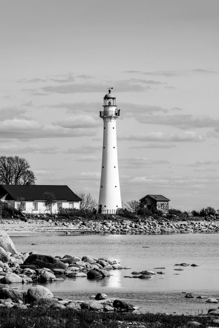Black and white image of a lighthouse by a rocky coastline, exuding a serene and timeless feel.