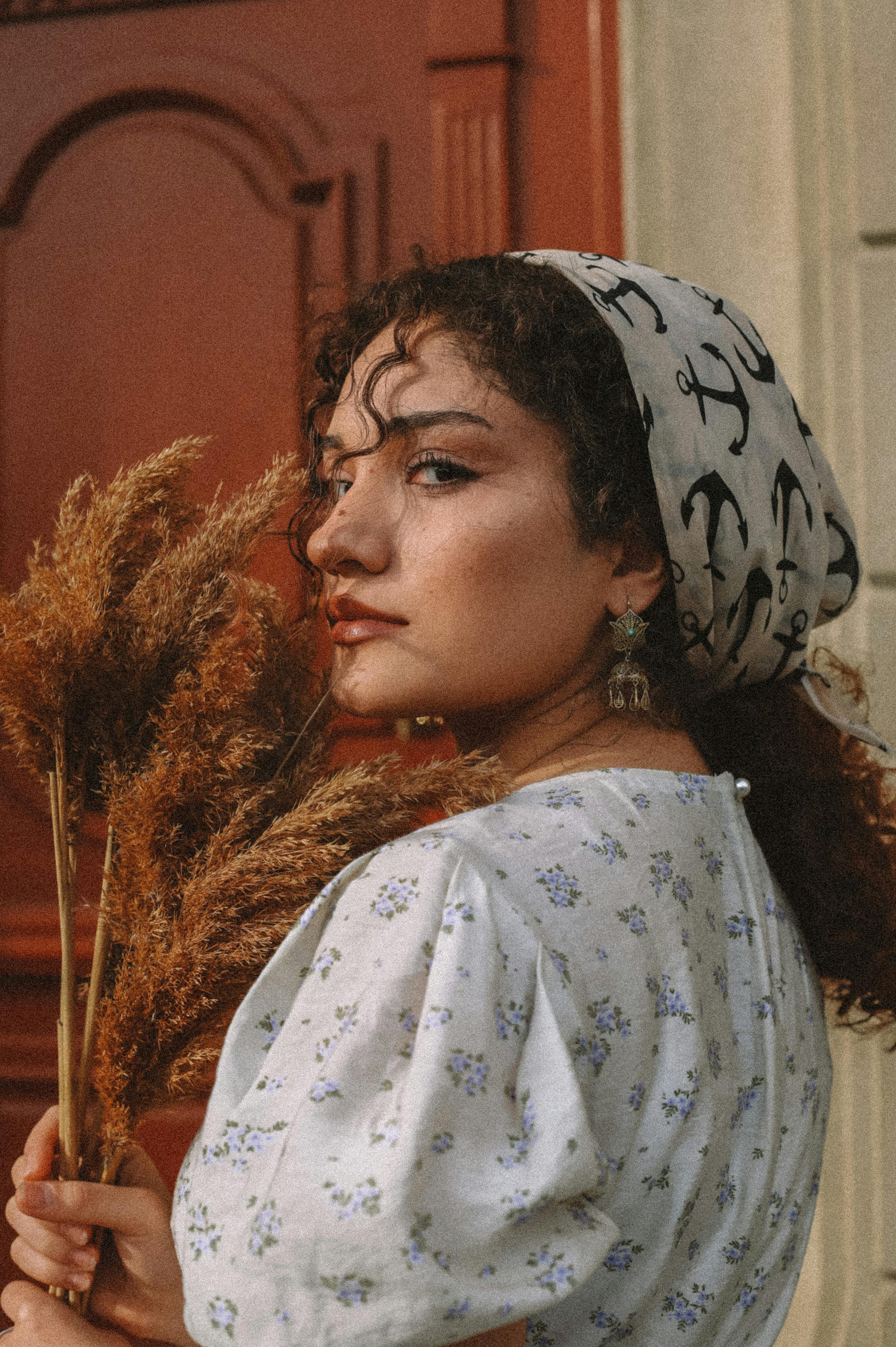 Aesthetic vintage portrait of a woman with a patterned headscarf and floral dress holding pampas grass.