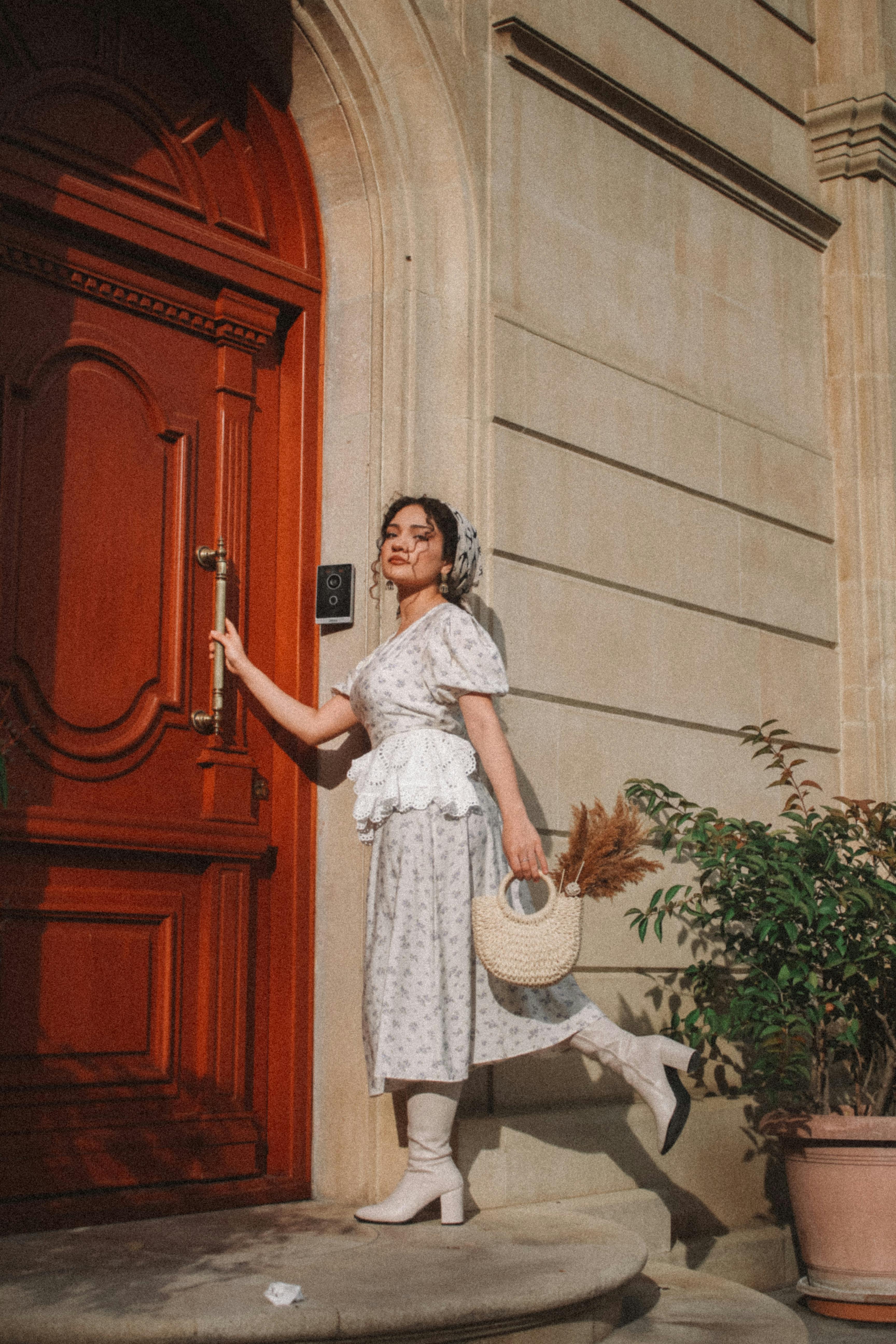 Elegant woman in vintage dress posing outdoors by a classic red door.