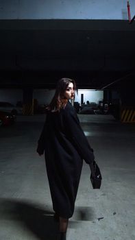 Woman in a dark coat turning in an urban parking garage, creating a mysterious and moody atmosphere.