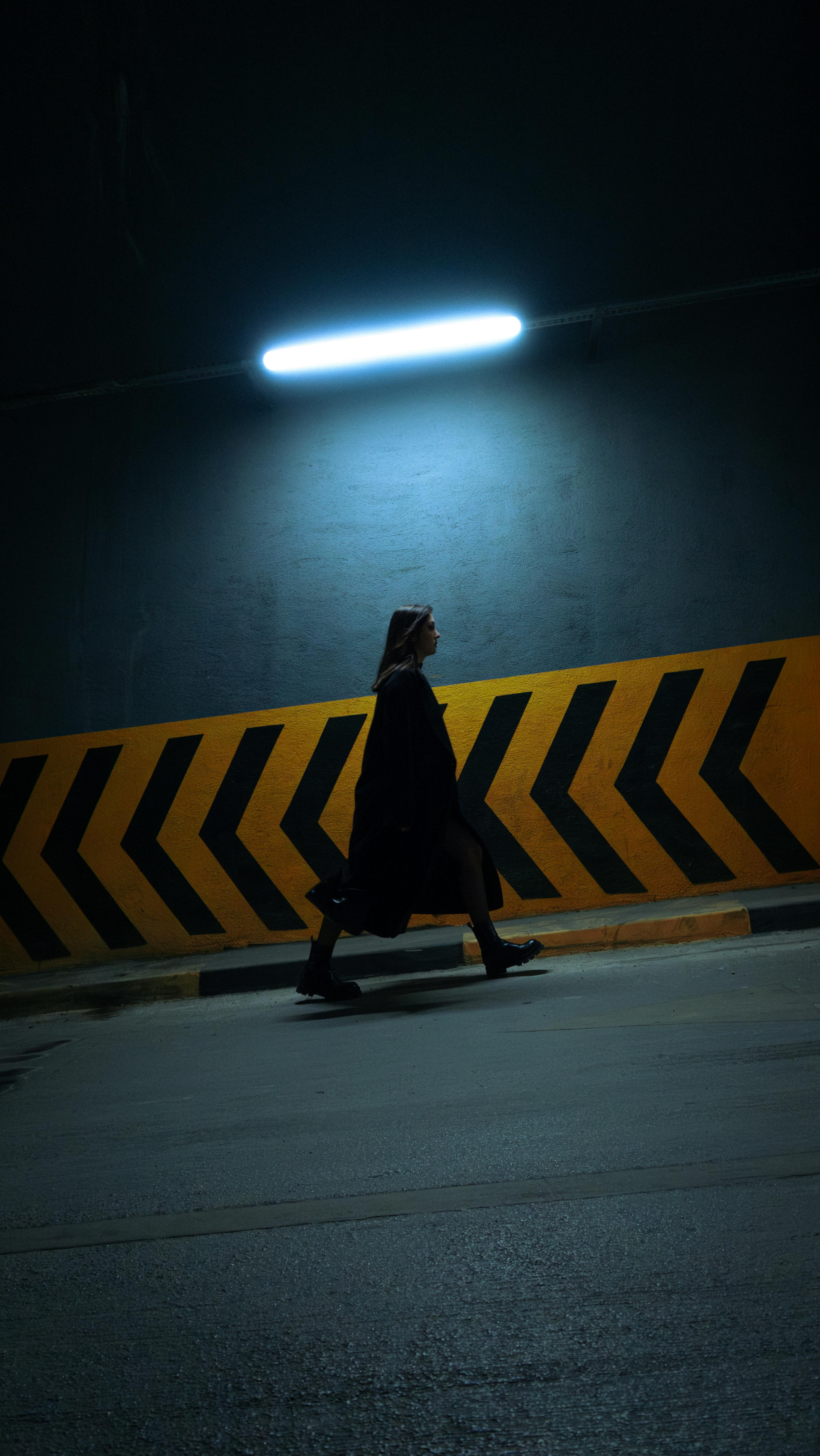 A woman walks through a dimly lit tunnel with chevron patterns, creating a mysterious urban atmosphere.