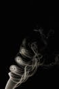 Whiff of thin white fume coiling and rising in dark room on black background