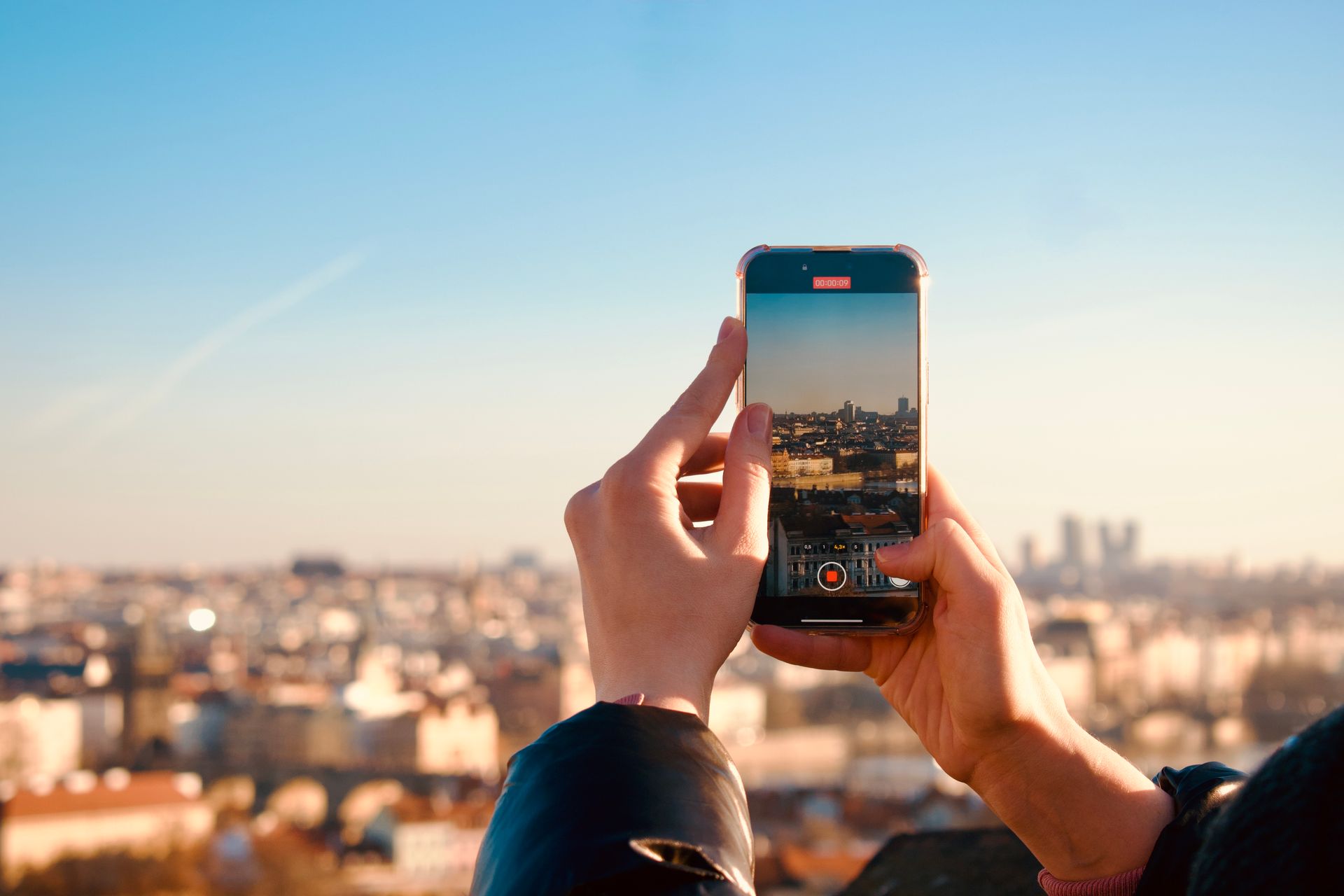 Hands holding a smartphone taking a photo of a city skyline during sunset, reflecting modern travel and technology.