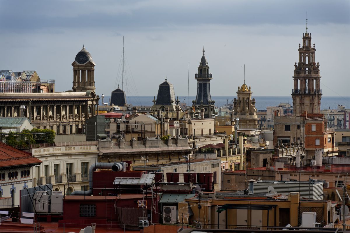 Priveliște peste acoperișurile istorice și turnurile-clopotniță din Barcelona, cu marea în fundal