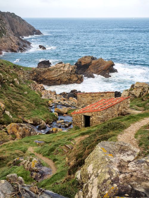 Free Rustic stone hut on the rugged coastline of Malpica, Spain, with crashing waves and rocky cliffs. Stock Photo