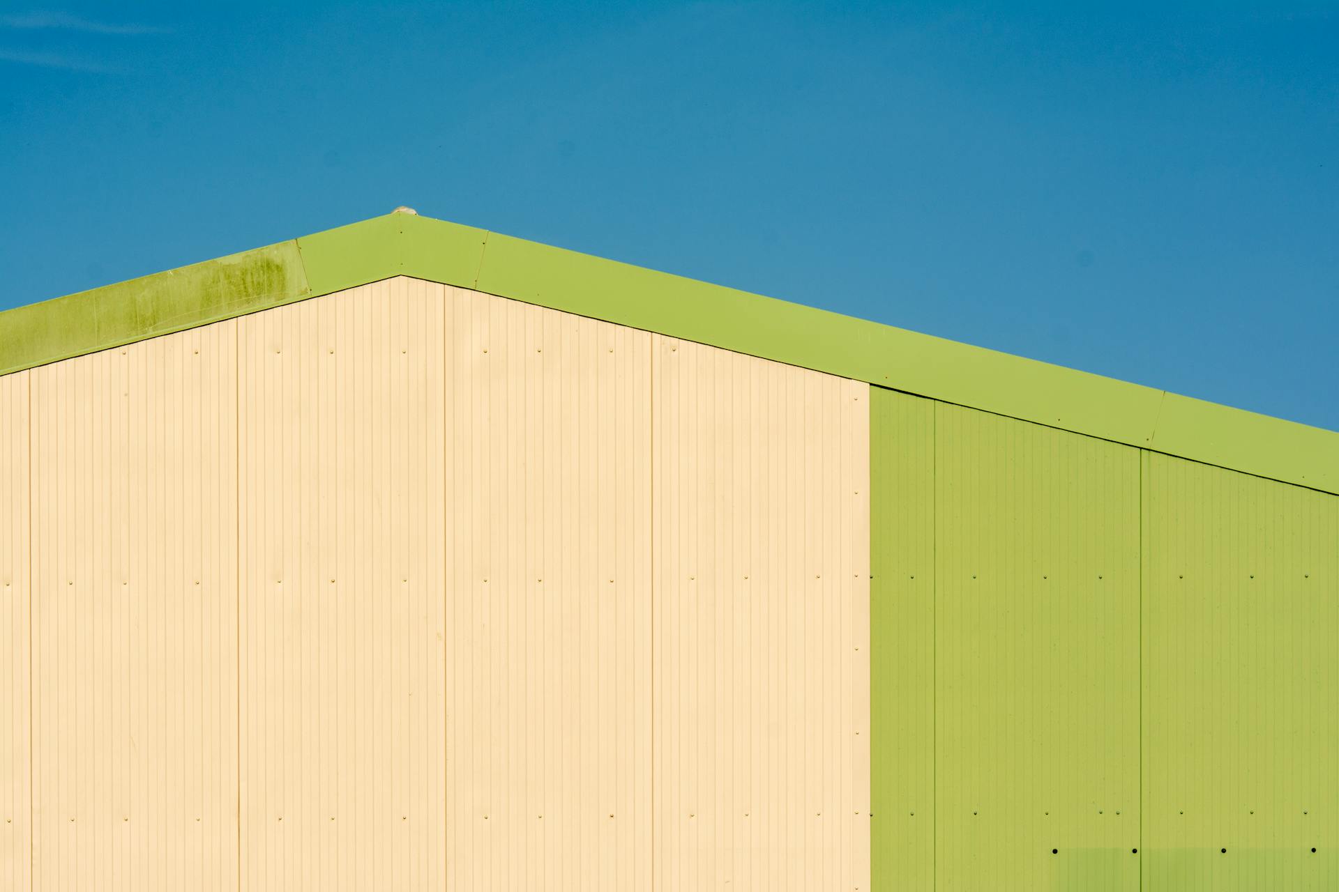 Minimalist warehouse facade featuring geometric design and contrasting colors under clear blue sky.