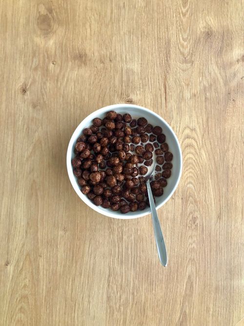 Free Top view of a bowl filled with chocolate cereal balls and milk, featuring a spoon, ideal for breakfast themes. Stock Photo