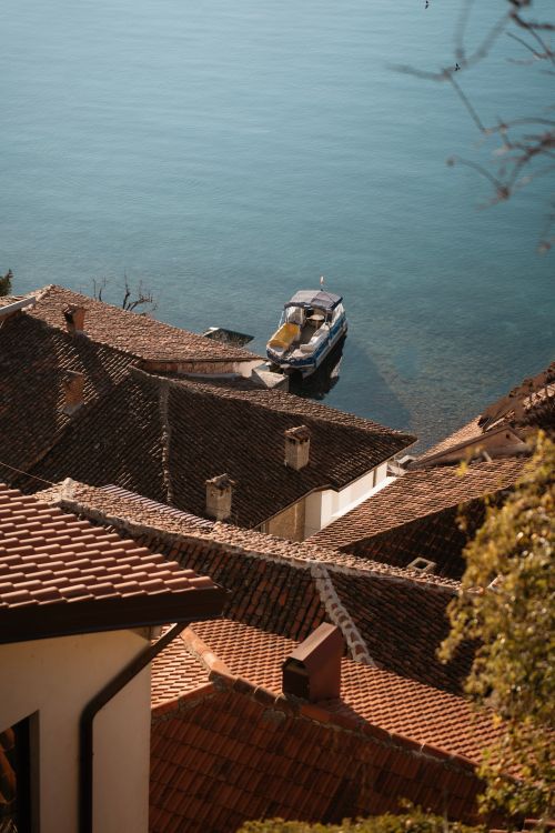Free Charming view of a boat by Lake Ohrid with terracotta rooftops in the foreground. Stock Photo