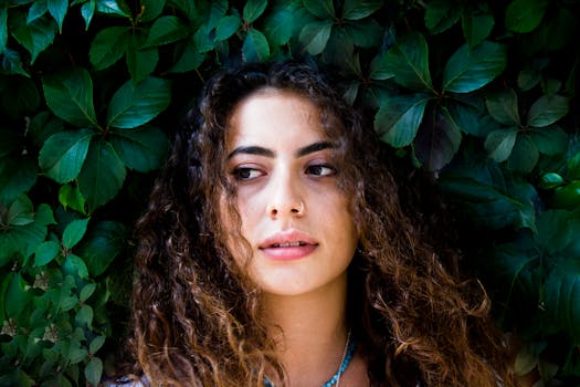 一位年轻卷发女子的特写肖像，背景是充满活力的绿叶