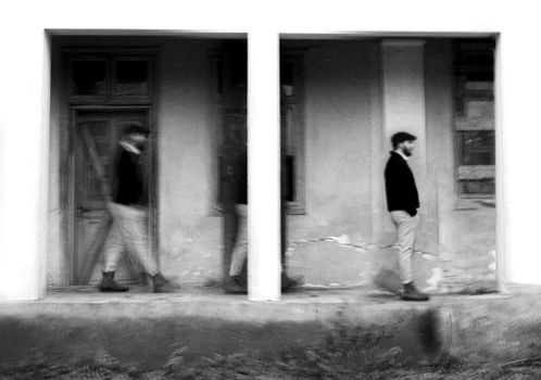 A creative black and white motion blur of a person walking in front of a building.