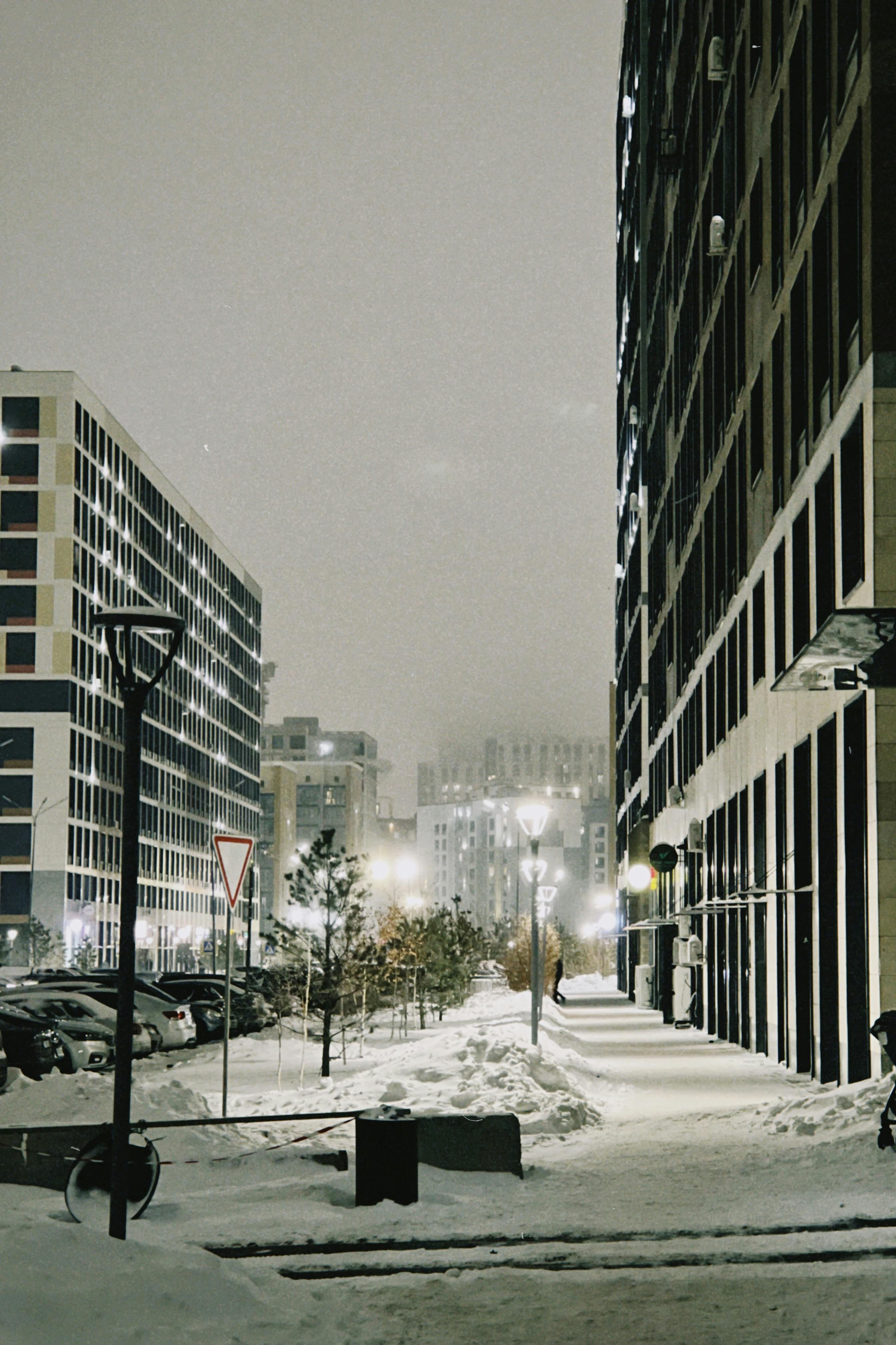 A serene snowy street scene in Astana, Kazakhstan at night, showcasing modern architecture under soft lights.