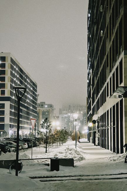 A serene snowy street scene in Astana, Kazakhstan at night, showcasing modern architecture under soft lights.