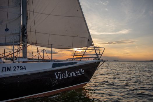 Sailboat with name Violoncelle gliding under sunset sky on Minsk Sea in Belarus.