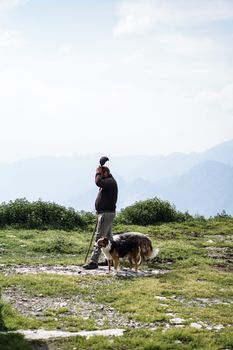 在一个晴朗的日子，一个人与牧羊犬走过风景秀丽的山区