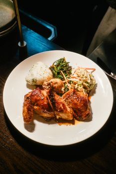 Gourmet roasted chicken with sesame seeds, rice, and vegetables on a white plate.