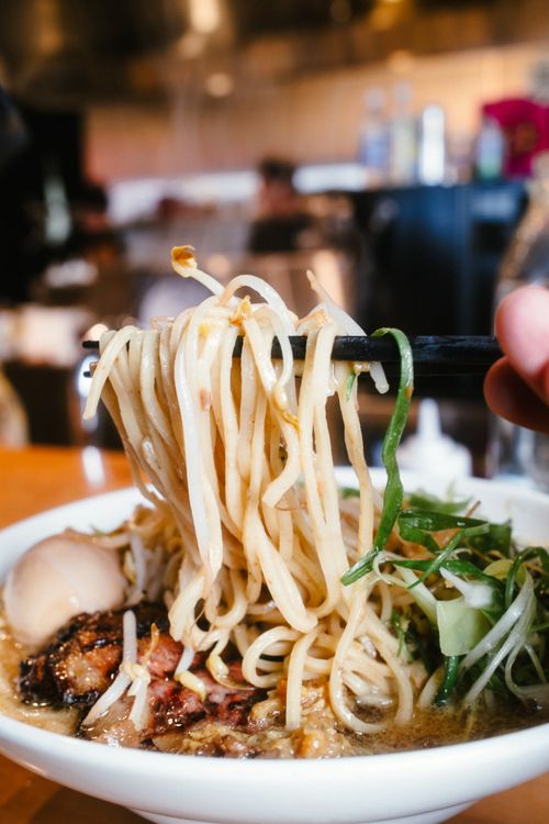 Free Mouthwatering close-up of ramen bowl with chopsticks in a lively restaurant setting. Stock Photo
