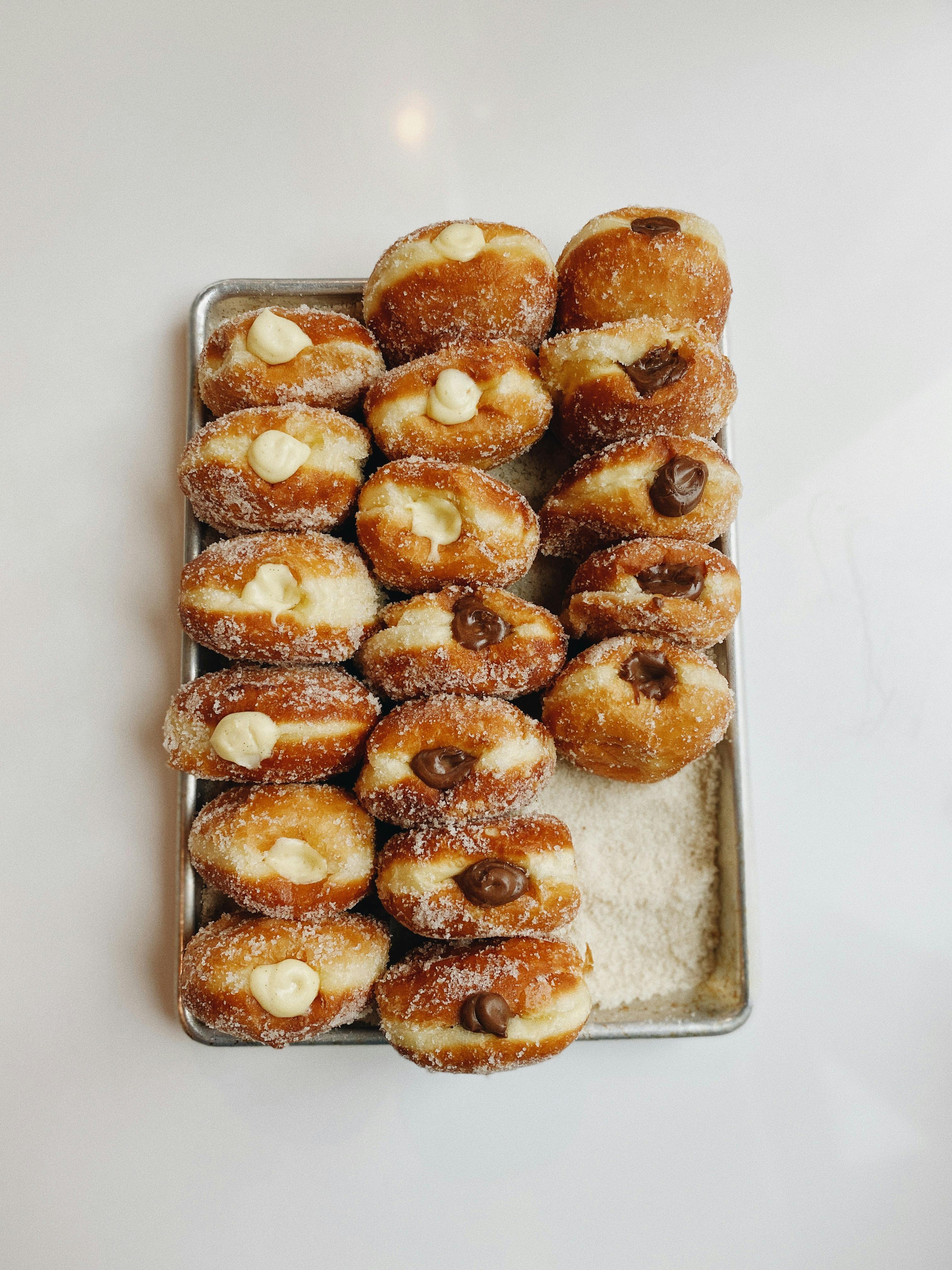 Fresh artisan doughnuts filled with vanilla and chocolate cream on a tray.
