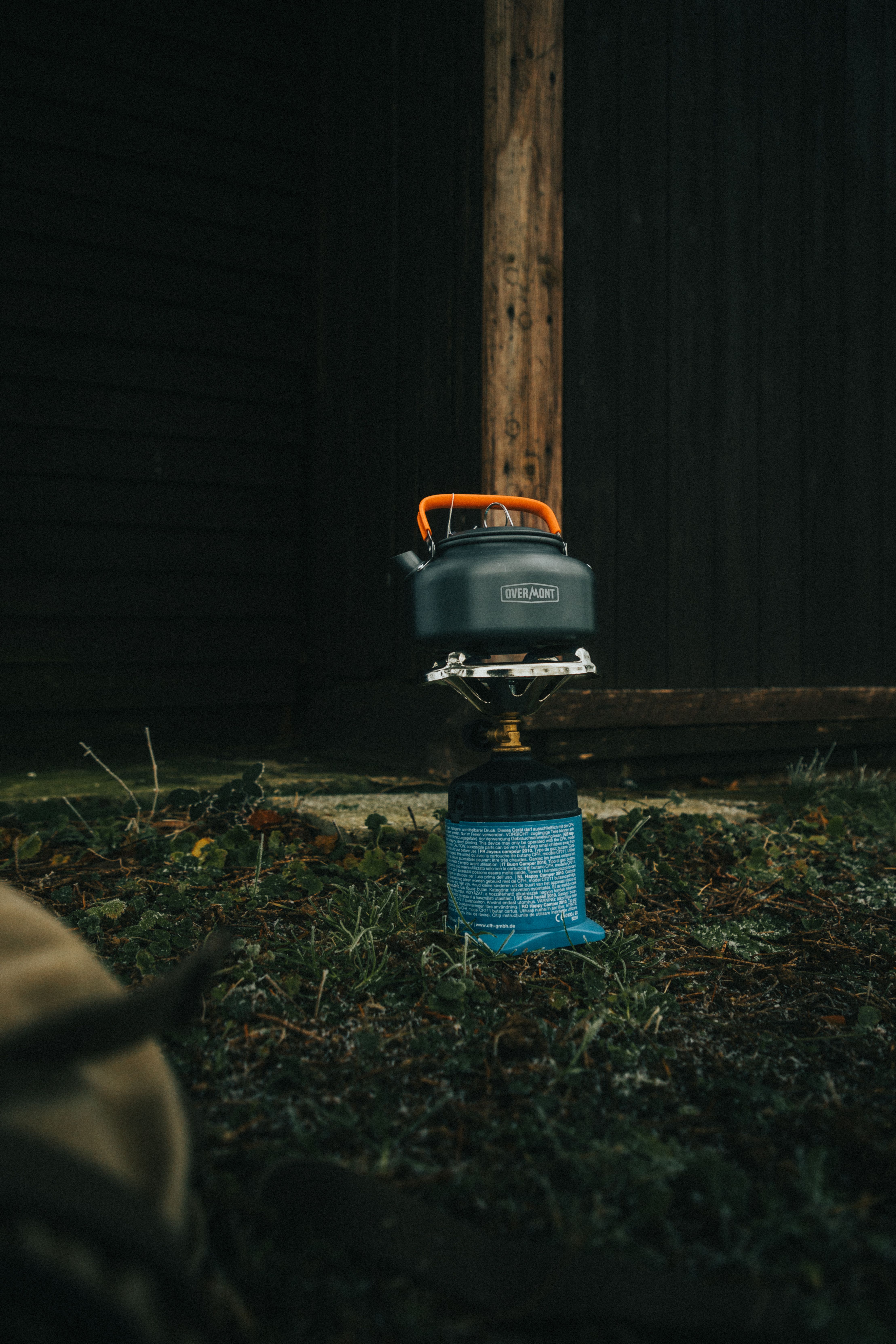 Compact backpacking canister stove on a flat rock with a small pot and fuel canister, forest campsite background