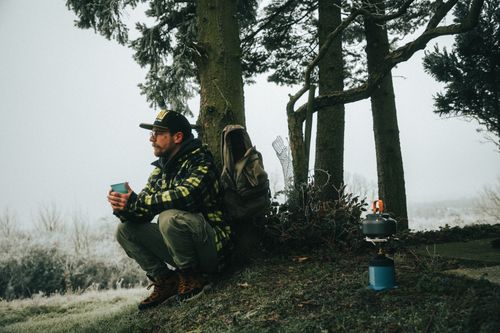 Free A man enjoys a hot drink in a foggy winter forest setting, equipped for bushcraft camping. Stock Photo