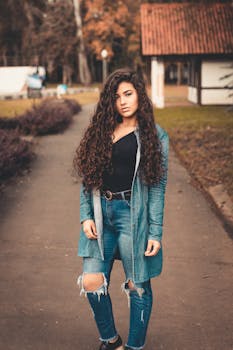 一位卷发的年轻女子穿着牛仔服装，在户外小路上摆姿势