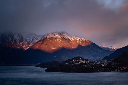 Free A breathtaking view of mountains at sunset with dramatic lighting and water in the foreground. Stock Photo