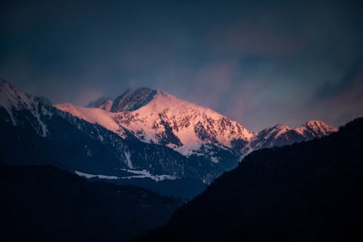 Dramatic sunset lighting on snowy mountains creates a breathtaking landscape view.