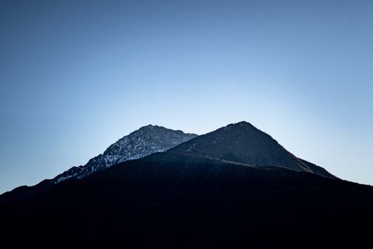 A serene mountain silhouette captured against a clear blue sky at dawn.