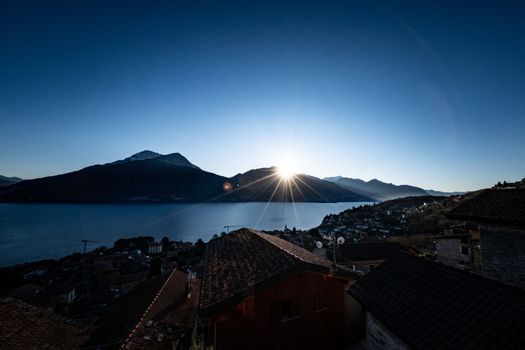 Dramatic sunrise over a serene mountain lake with scenic village rooftops in the foreground.
