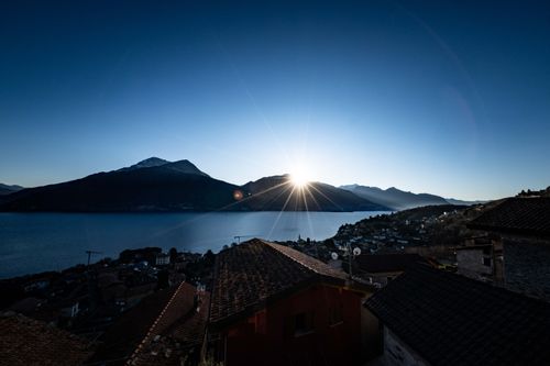 Free Dramatic sunrise over a serene mountain lake with scenic village rooftops in the foreground. Stock Photo