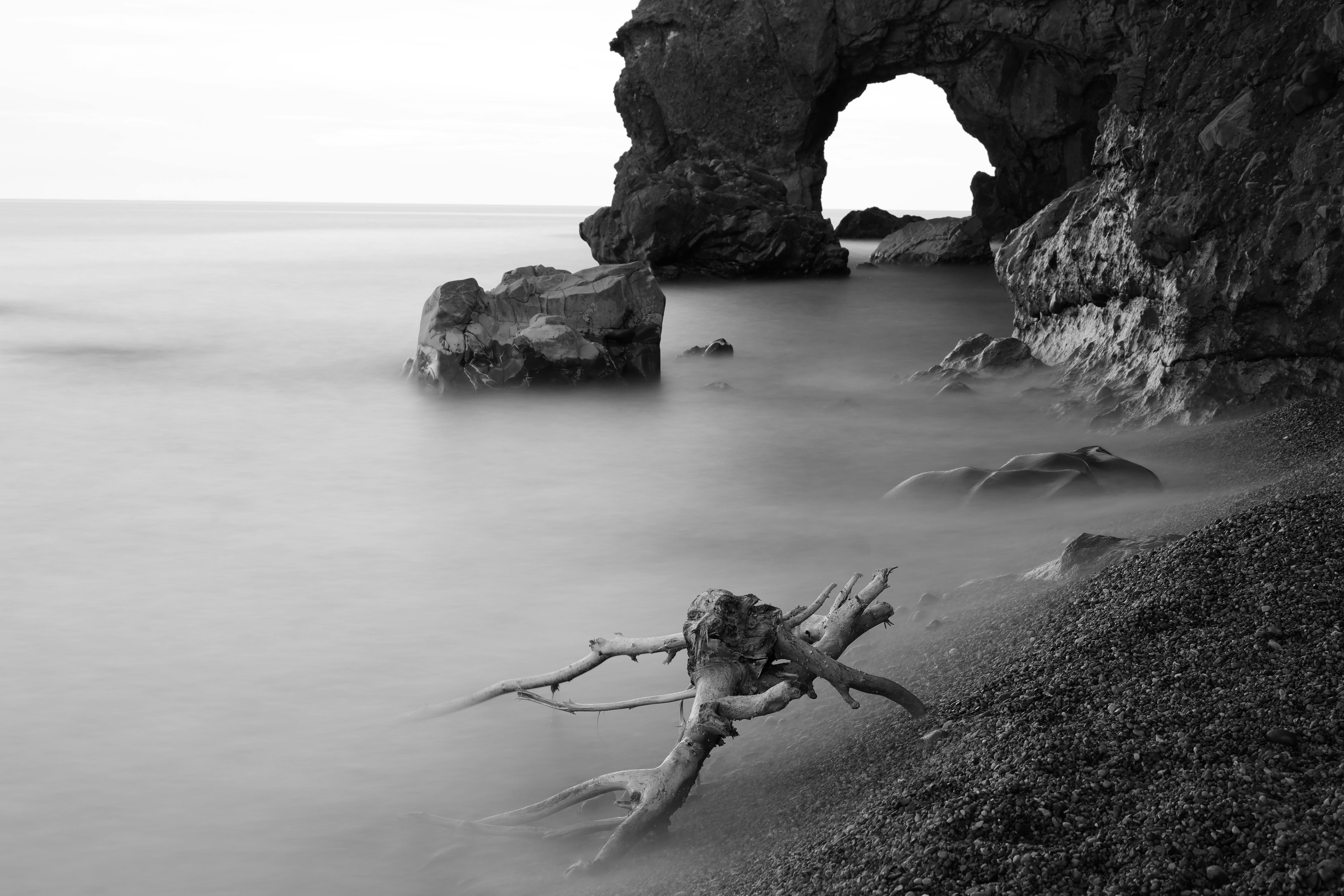 A serene black and white seascape with rocky arch formations.