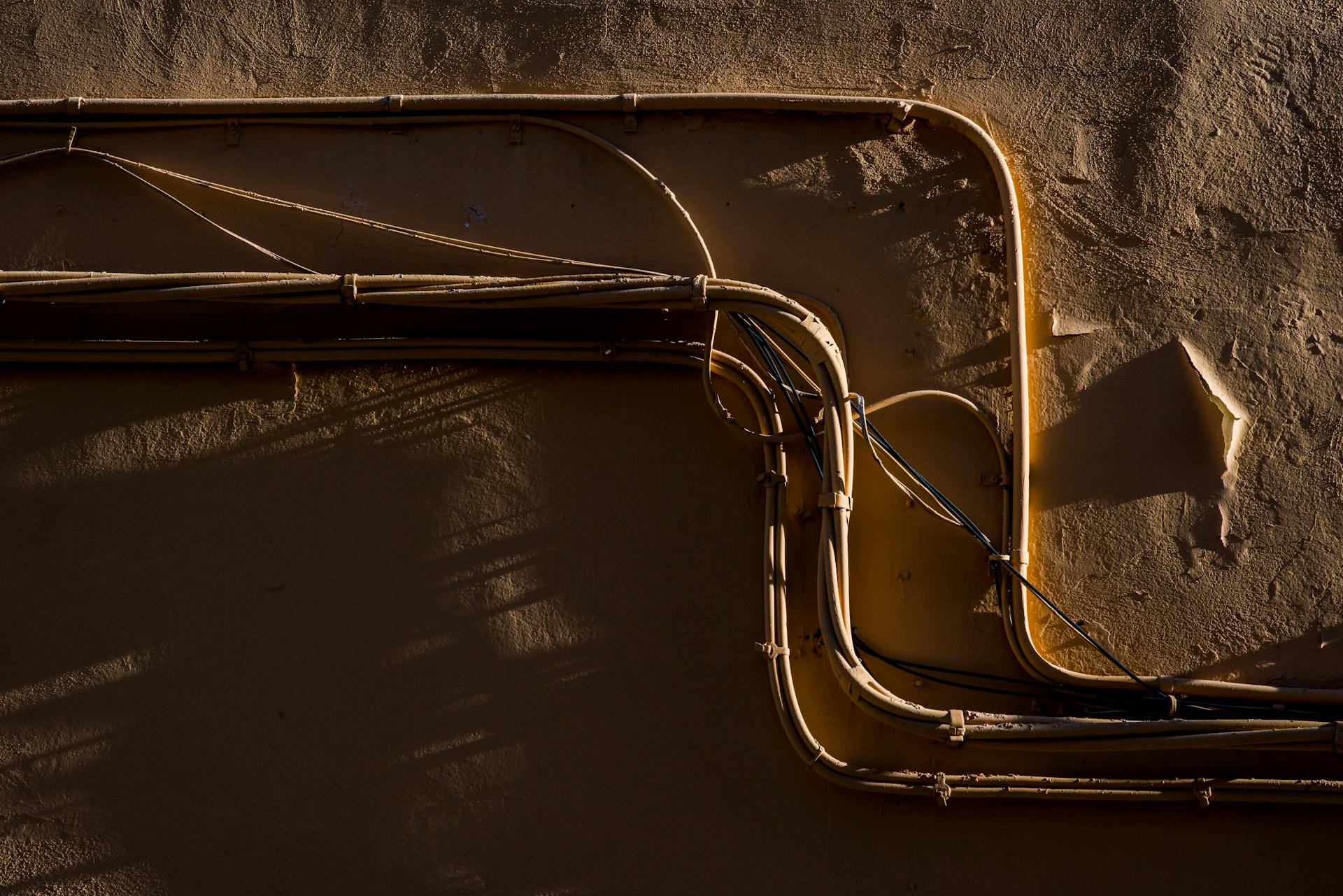 A textured wall featuring exposed electrical conduits casting dramatic shadows.