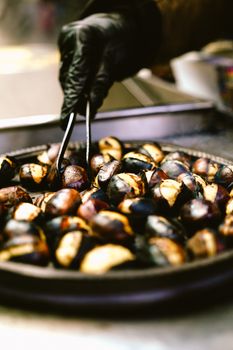 Black-gloved hand picking freshly roasted chestnuts from a pan.