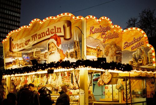 Free Illuminated Christmas market stall in Berlin showcasing traditional sweets and festive decor. Stock Photo